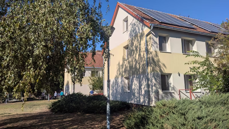 Az Ezüstfenyő Idősek Otthona épülete a zöld, fás kertből nézve
